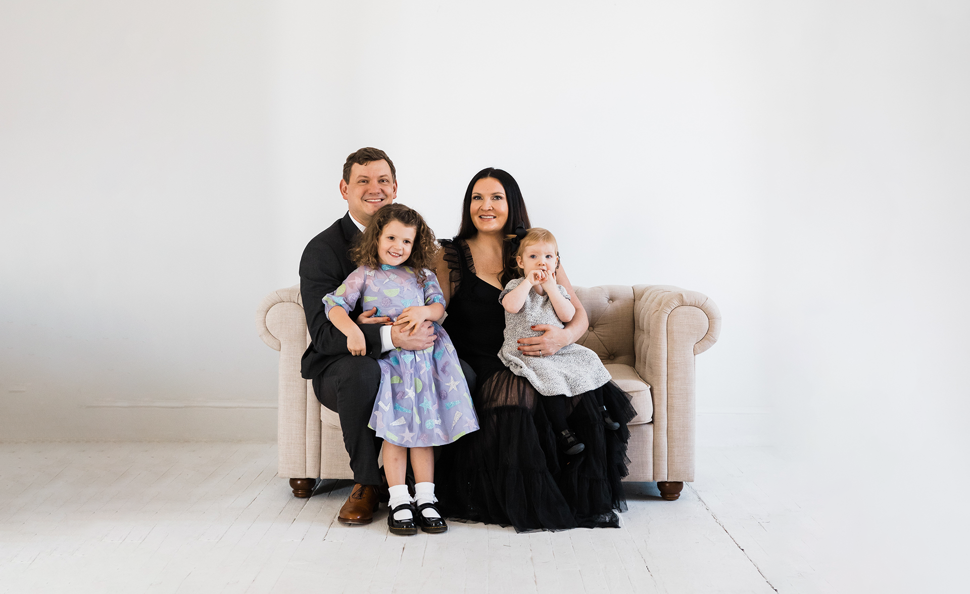 A couple poses on a love seat with their two children