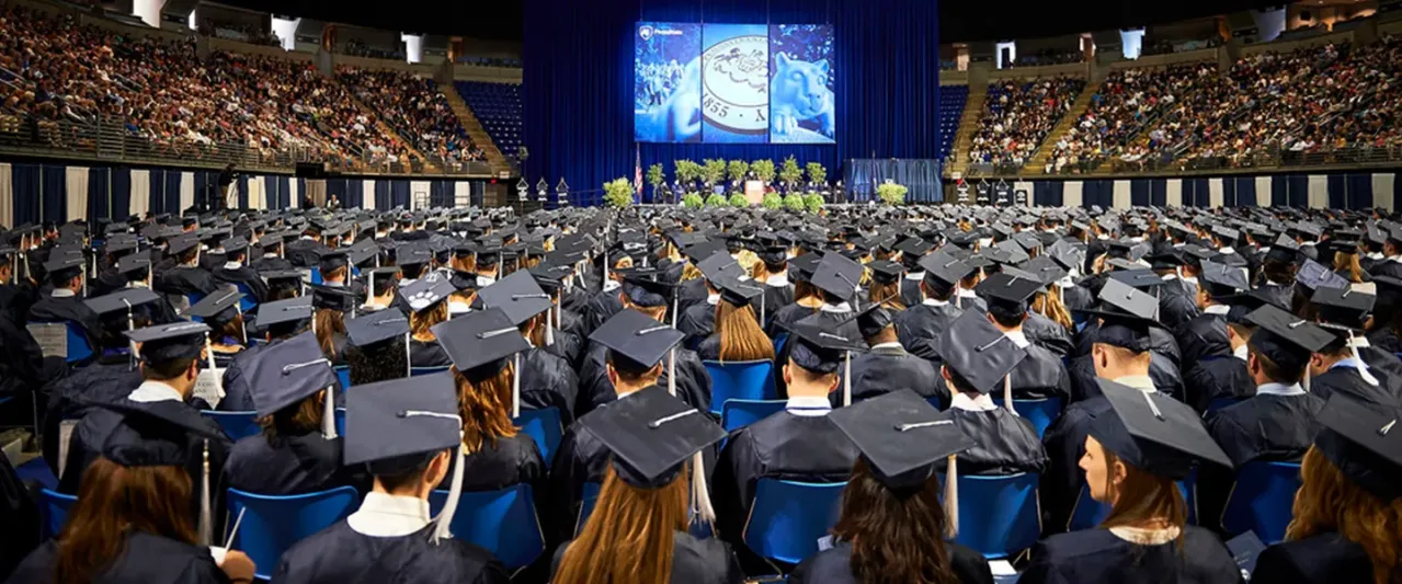 View of Penn State Commencement ceremony taking place in the Bryce Jordan Center. Rows of students dressed in caps and gowns.