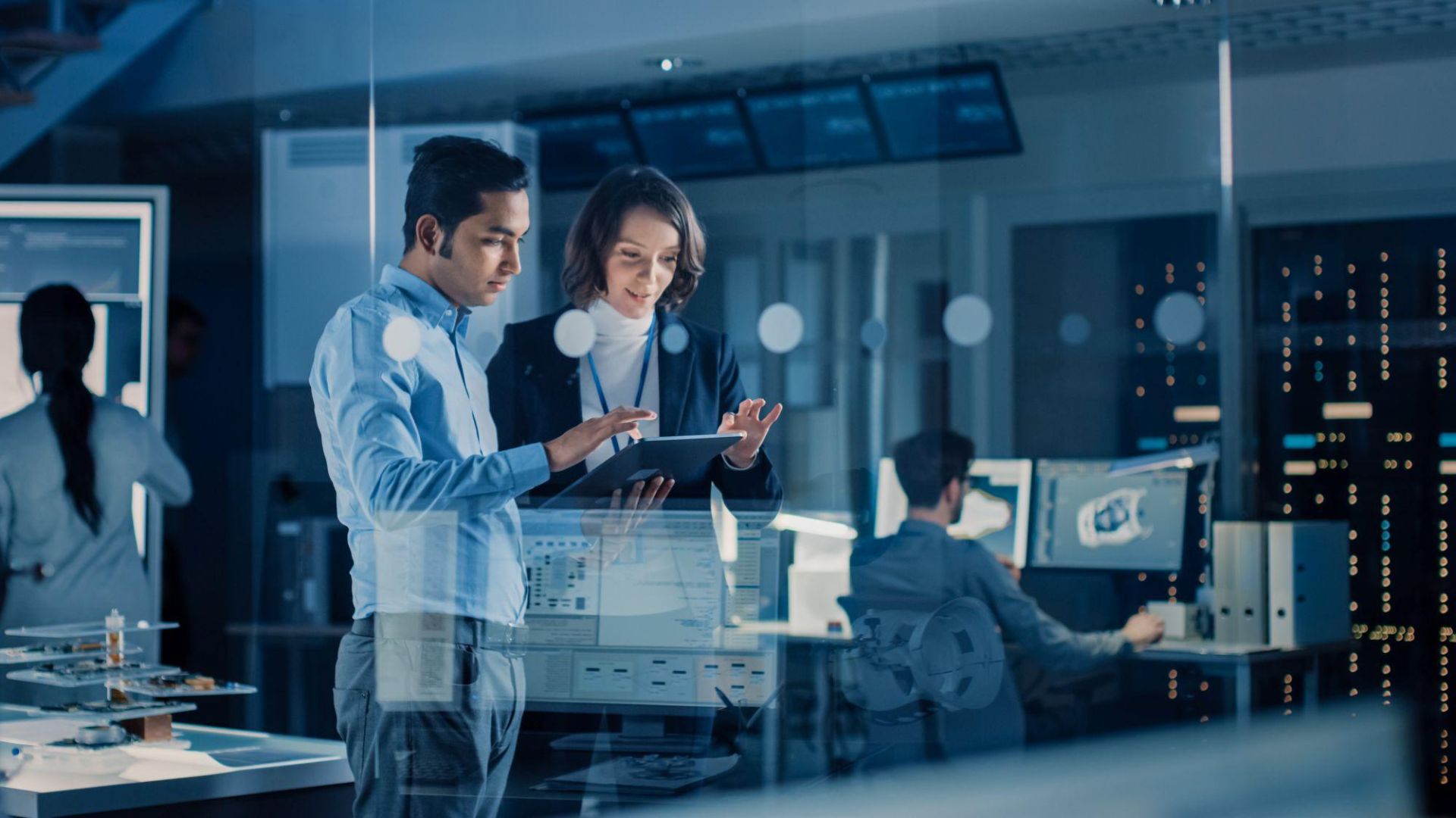 Two people look at a tablet in a technology design facility.
