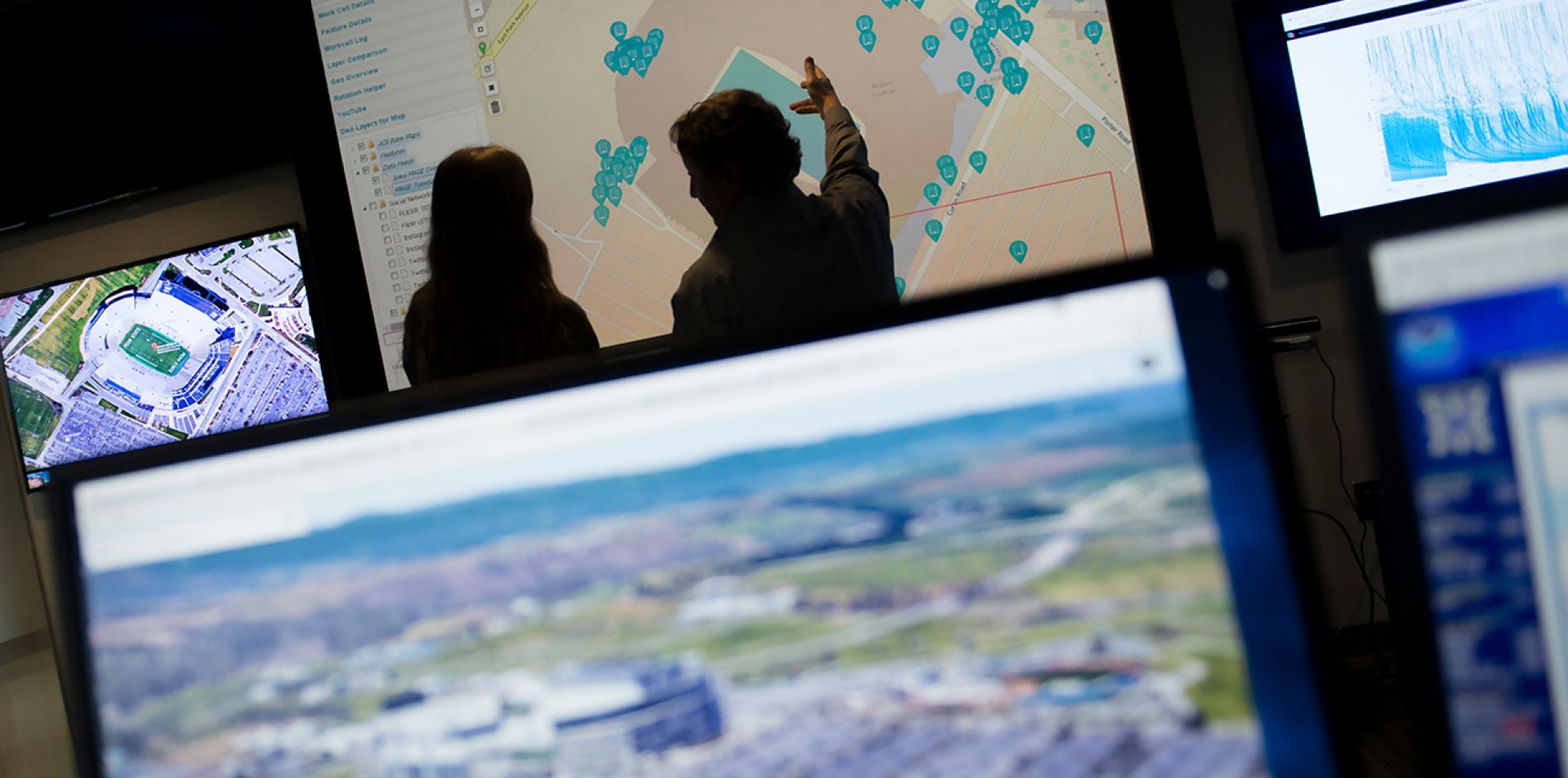 Two people review a map visualization on a large screen.