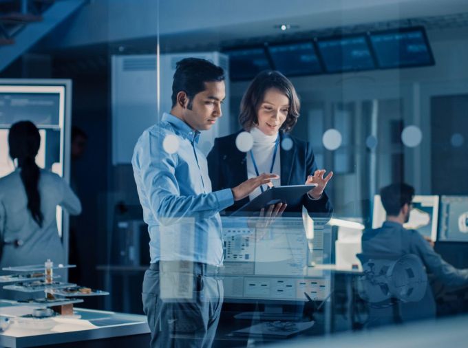 Two people look at a tablet in a technology design facility.