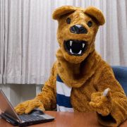Penn State Nittany Lion mascot using a laptop.