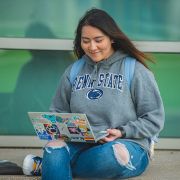 Young female student smiling outside with a laptop with many stickers on lid