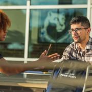Two students sit at a table with laptops having a discussion