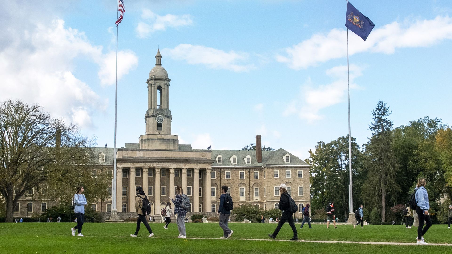 Students walk across Penn State's University Park campus in front of the Old Main building.