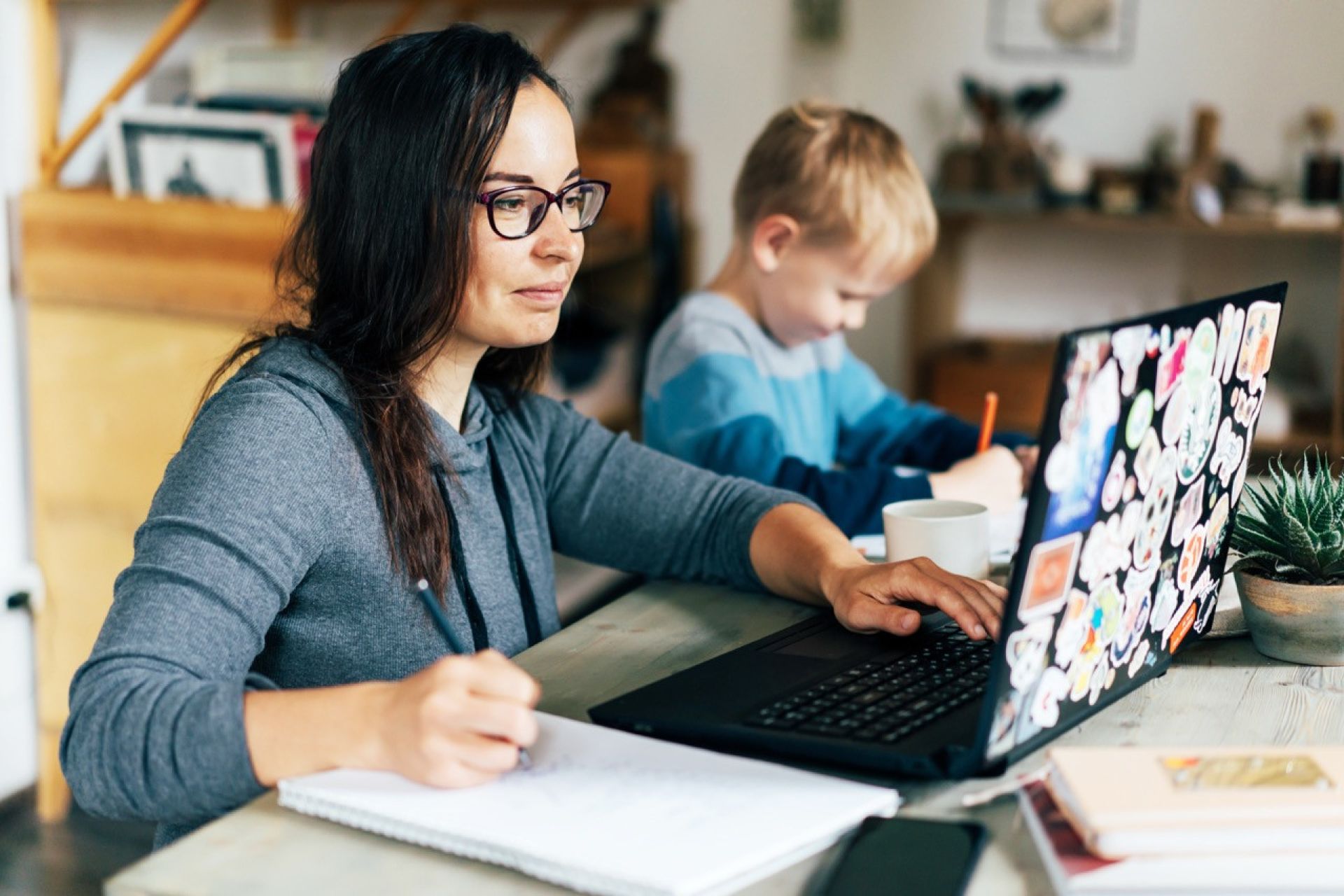 Adult student learning online, working on school work at home beside child.