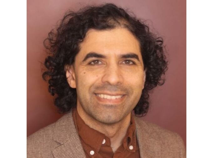 headshot of person with black curly hair and brown suit