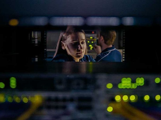 Student in data center through opening in back of server rack