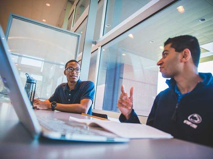 Two male students working at a desk with laptops