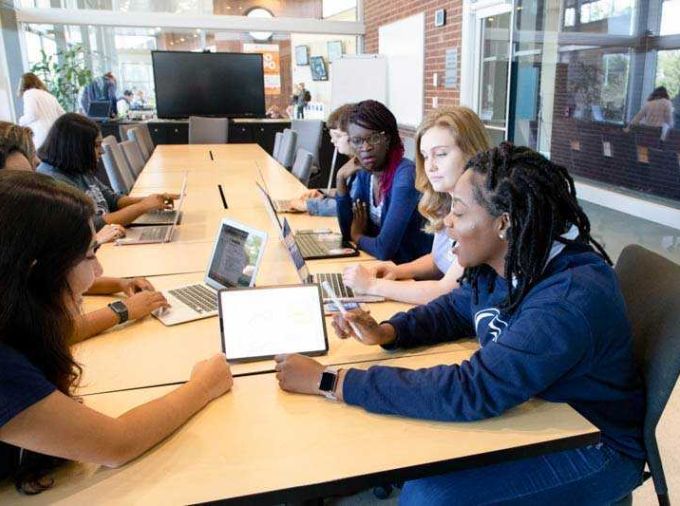 Six students with laptops gathered around a conference table