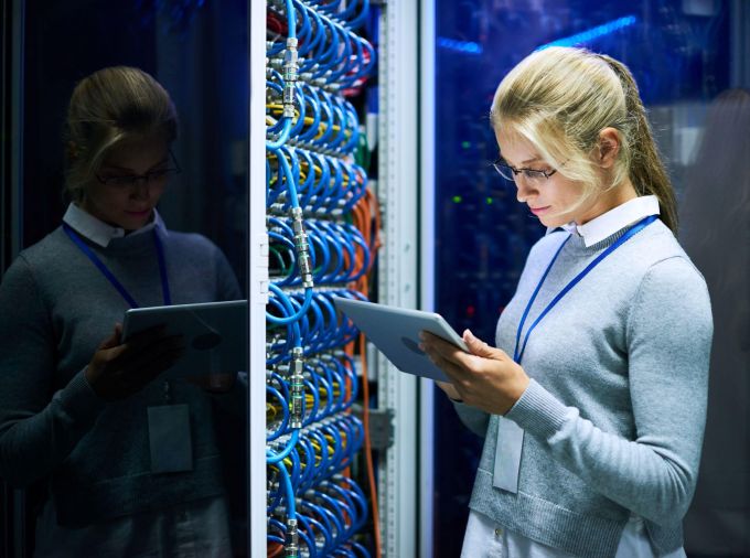 A person looks at a tablet in a server room.