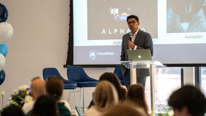 A faculty member speaks into a microphone in front of an audience.