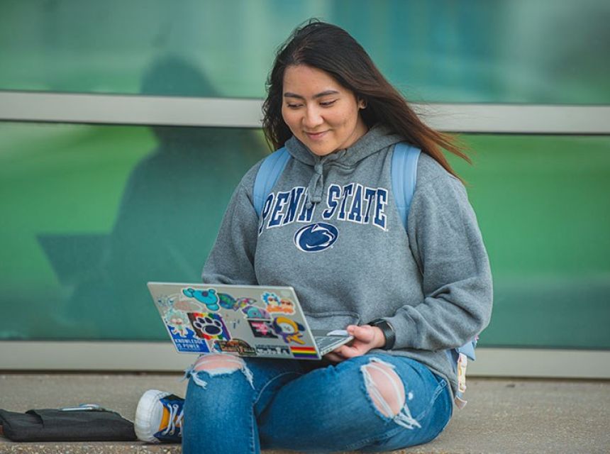 Young female student smiling outside with a laptop with many stickers on lid