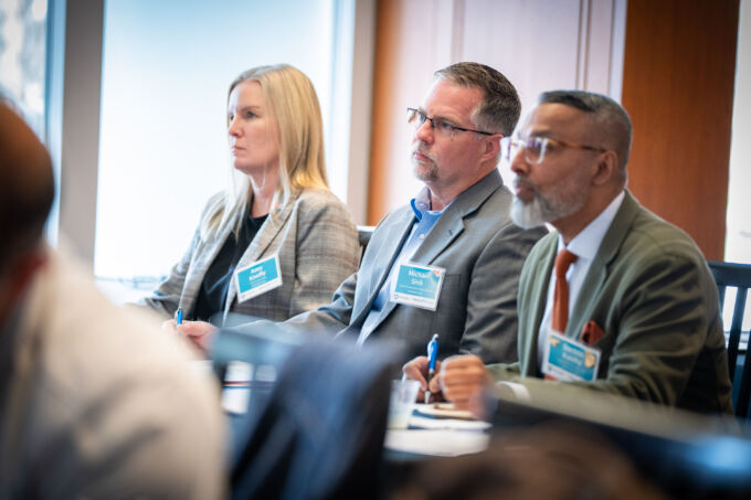 Three people sit at a table listening to a student presentation.