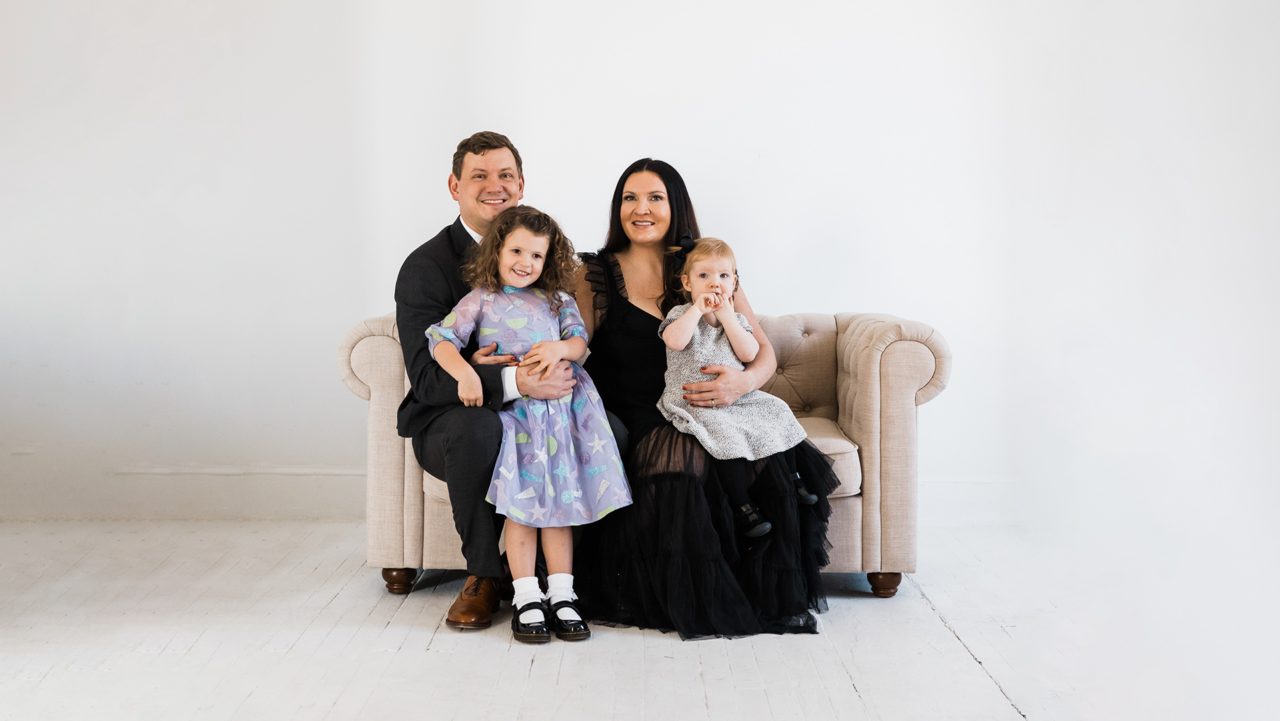 A couple poses on a love seat with their two children