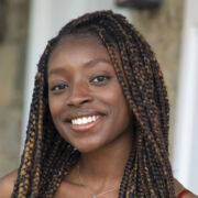 A woman with long braided hair smiles broadly while posing outdoors