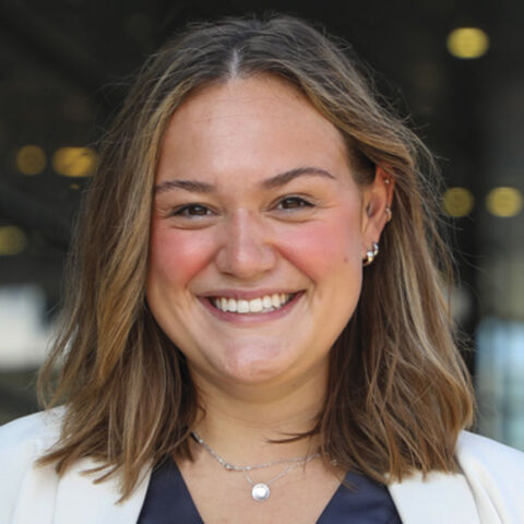 Young woman with shoulder-length brown hair smiles broadly in a navy shirt and white jacket