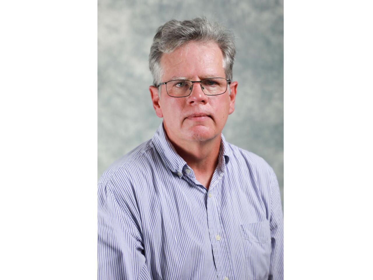 headshot of person with gray hair, wire-rimmed glasses, lavender dress shirt
