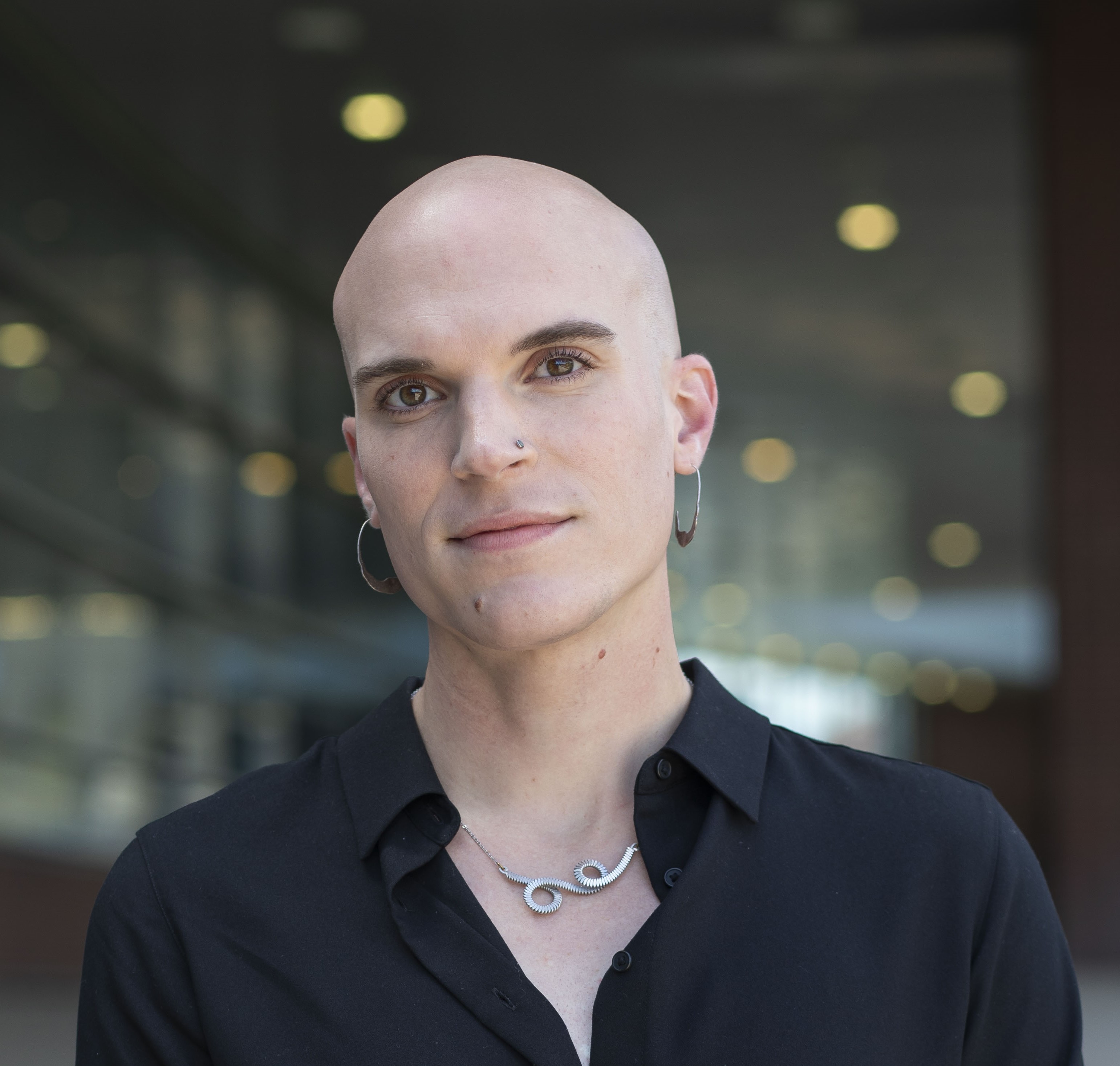 bald person in black attire with brick and glass building in background